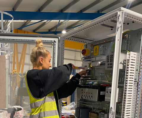 young female with screwdriver working on a large fuse box