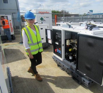 young female in high vis waistcoat stood next to an aggreko piece of equipment